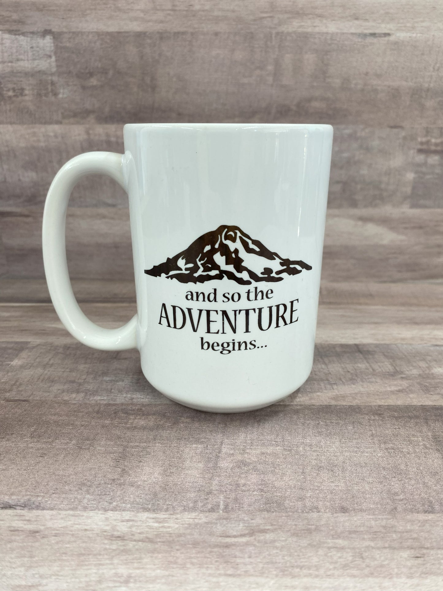 16oz ceramic mug, white base, with the phase and so the adventure begins with a artist image of Mount Rainier in black sublimated ink