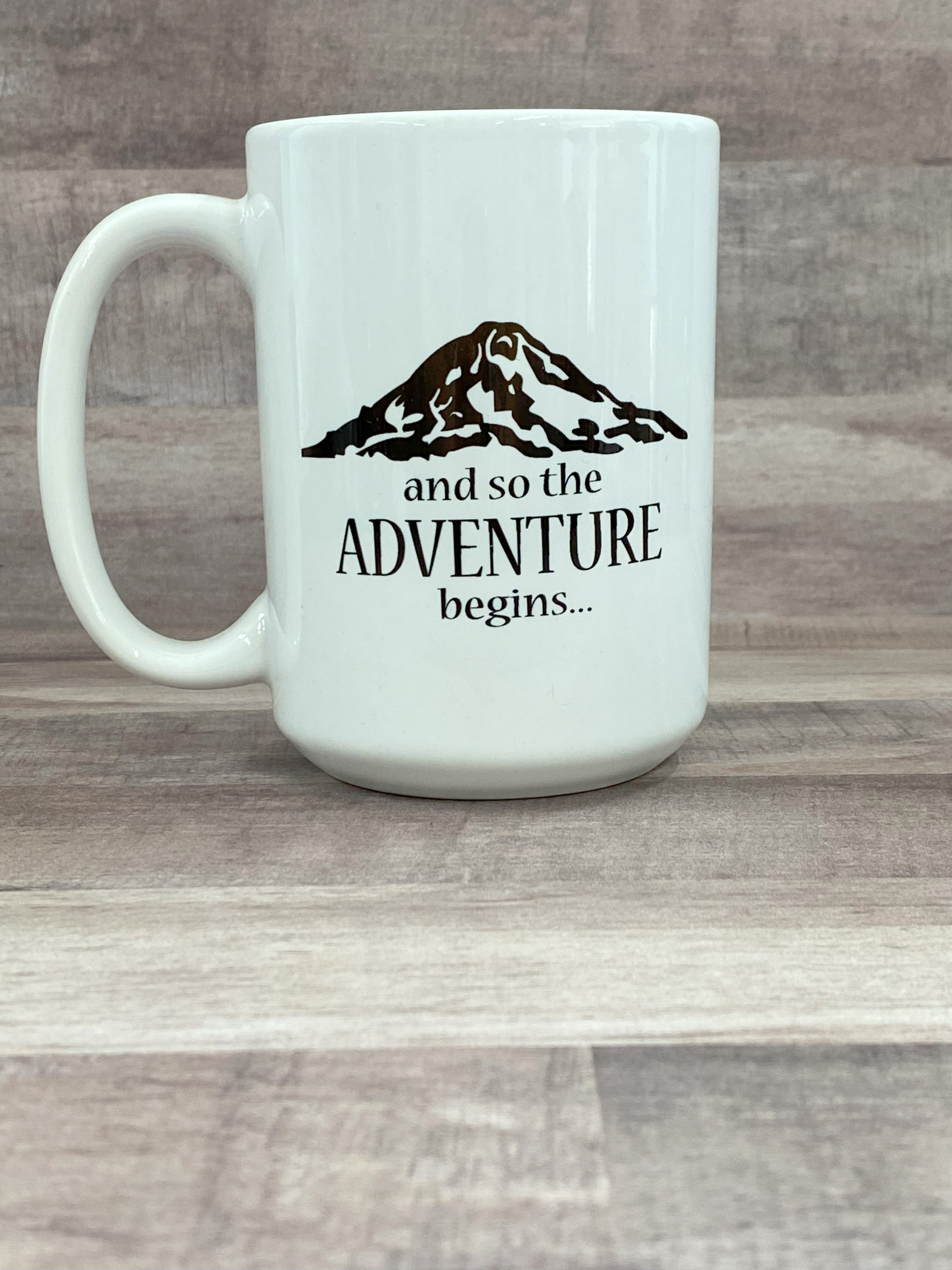 16oz ceramic mug, white base, with the phase and so the adventure begins with a artist image of Mount Rainier in black sublimated ink