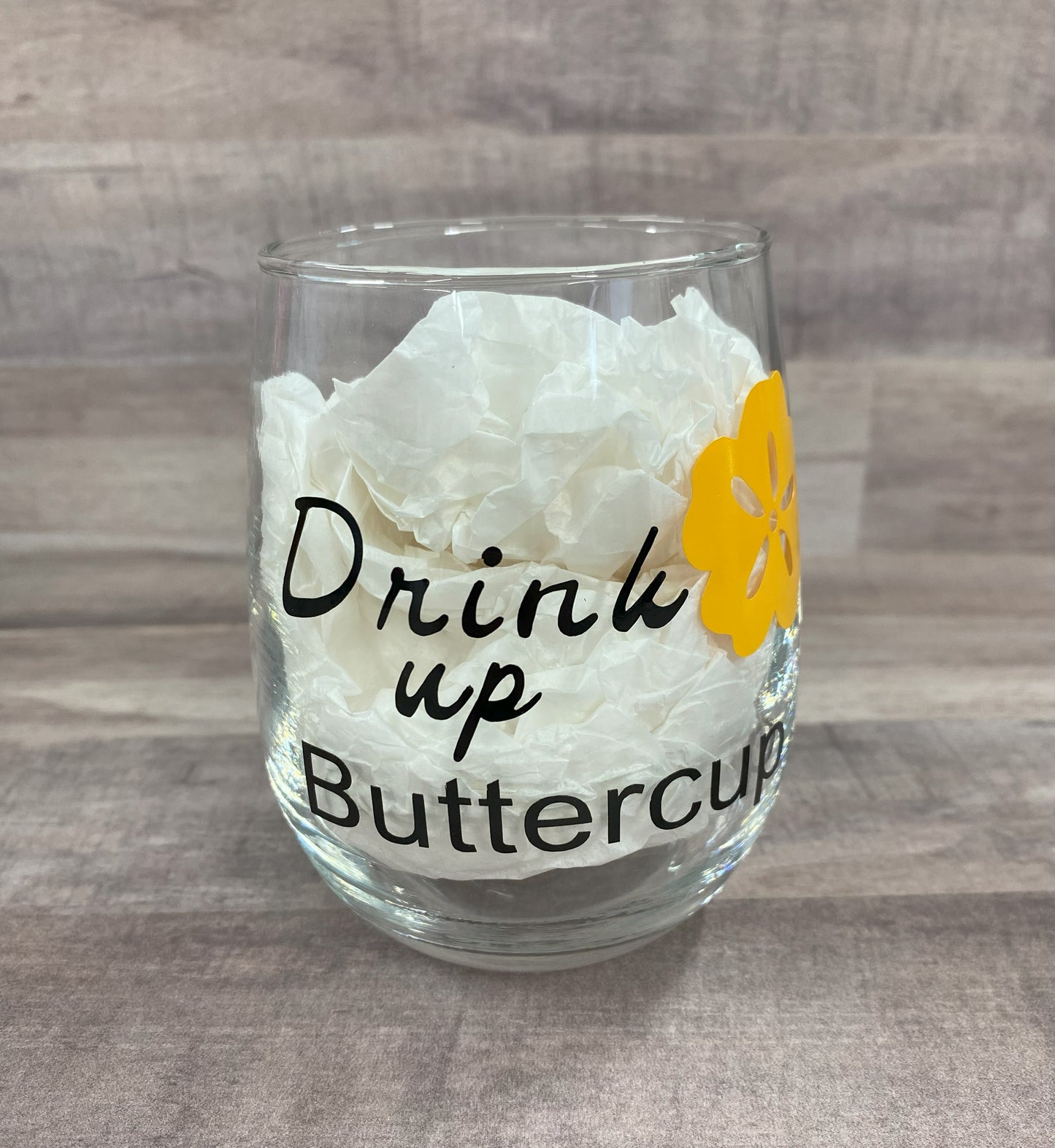 Stemless 15oz wine glass with the phrase drink up buttercup in black writing with a yellow flower. Customizable. Designed by Grit City Rebel.