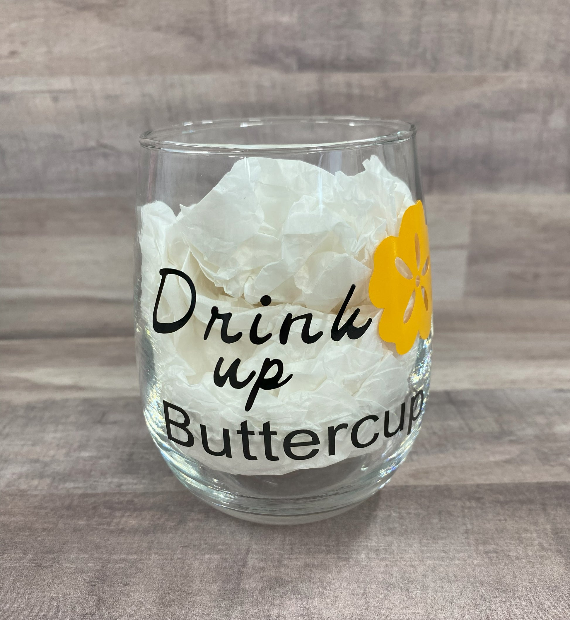Stemless 15oz wine glass with the phrase drink up buttercup in black writing with a yellow flower. Customizable. Designed by Grit City Rebel.