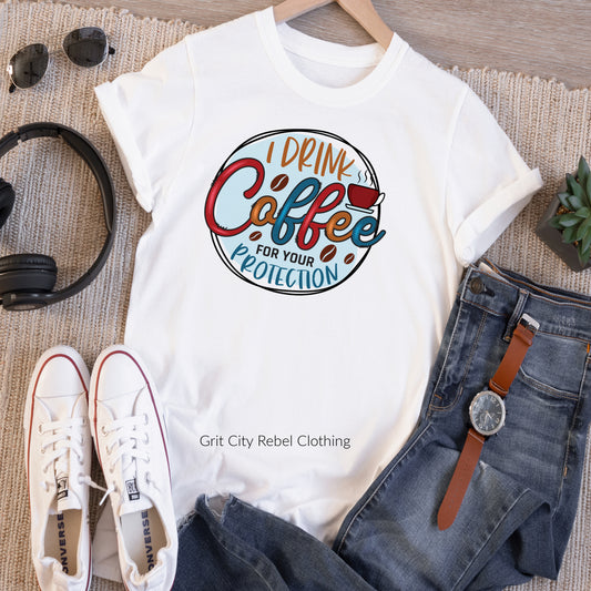 White unisex T-shirt with the saying I Drink Coffee For Your Protection in multi-colors Grit City Rebel sizing unisex sizes small medium large Xlarge 2X 3X
