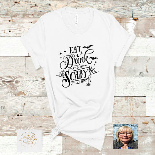 White short sleeve unisex T-Shirt with the saying Eat Drink and be Scary in black with bats and spider webs as accents