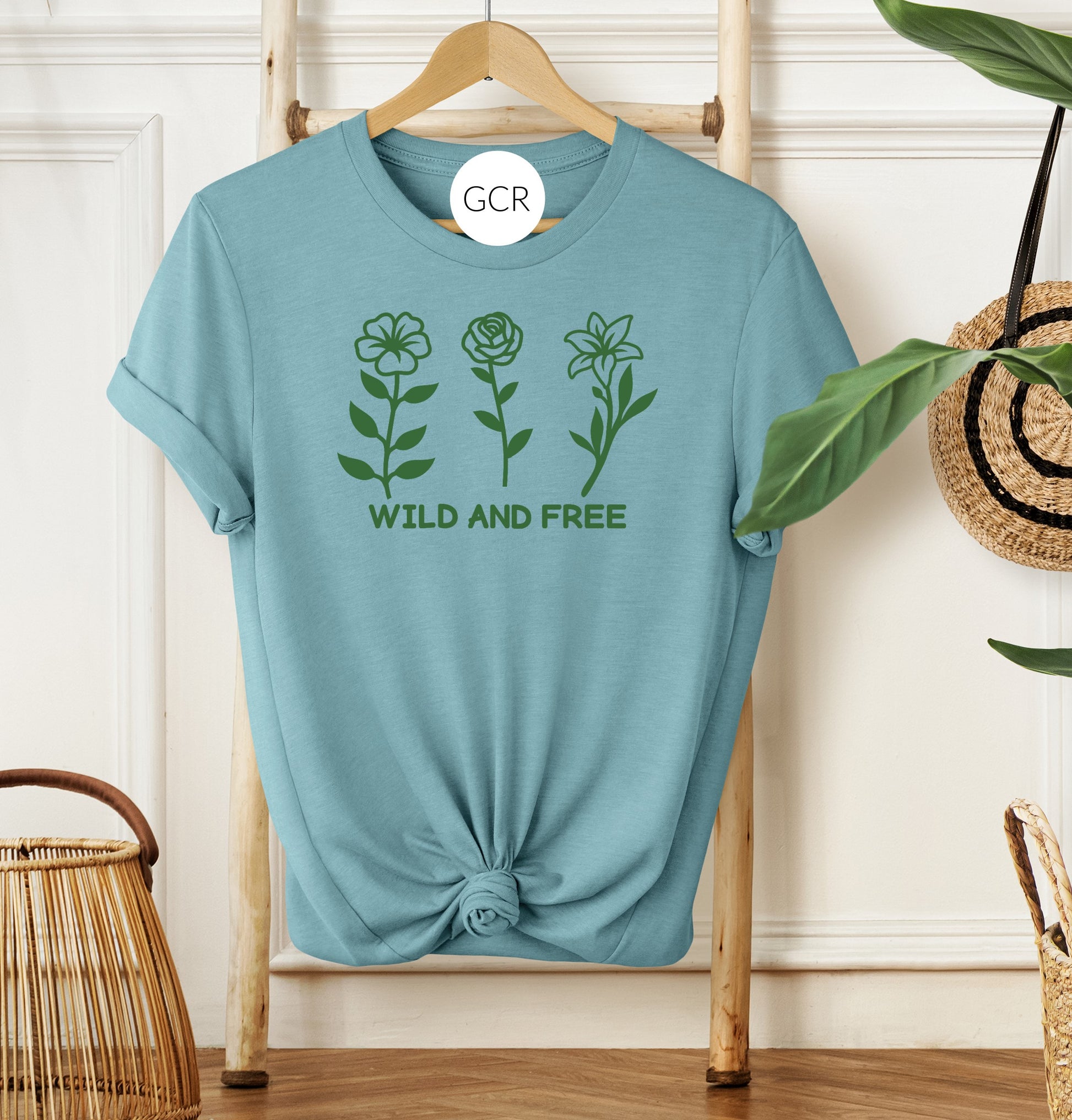 grit city rebel heather blue arctic unisex t-shirt with the phrase wild and free with a graphic of three flowers in a green vinyl