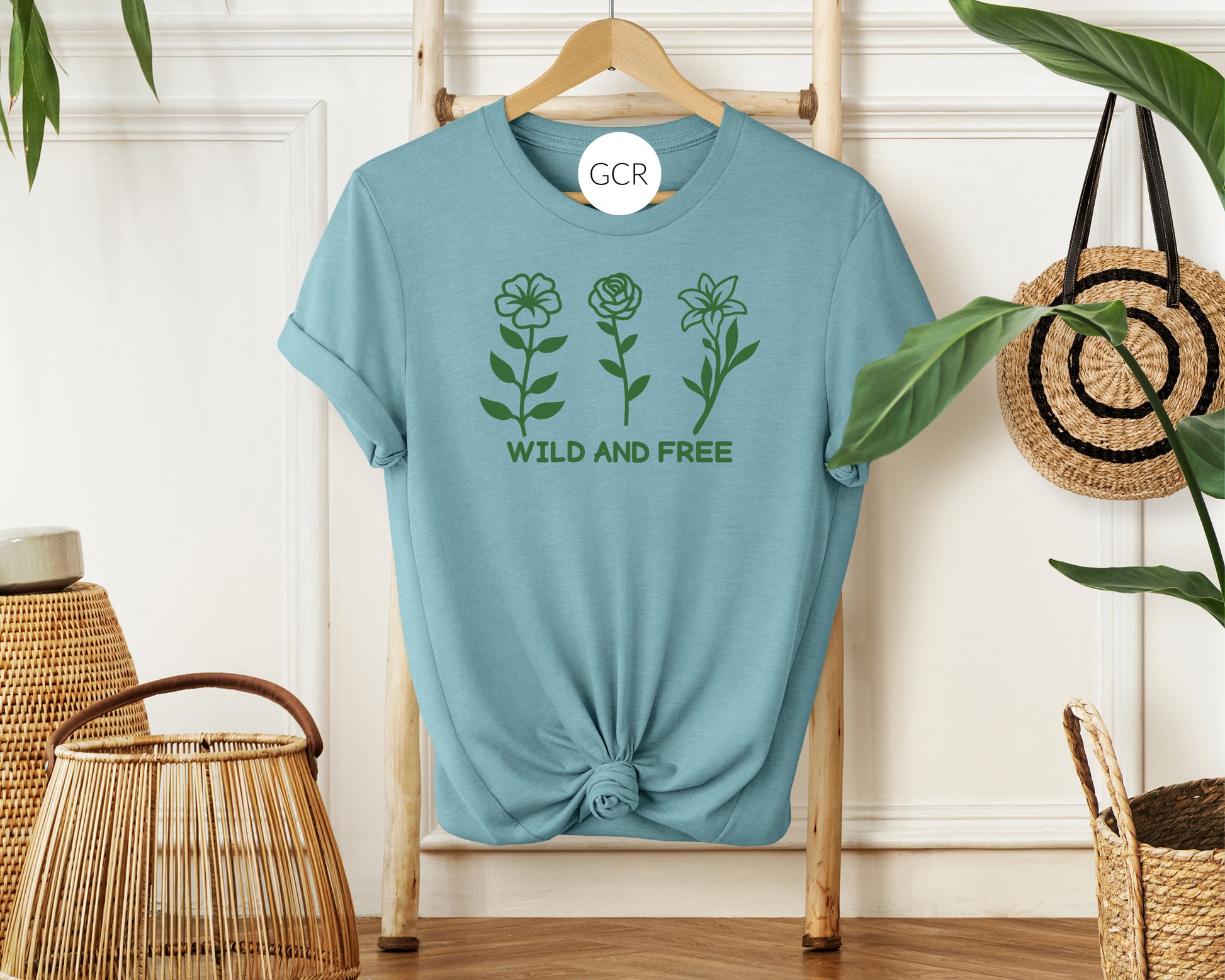 grit city rebel heather blue unisex t-shirt with the phrase wild and free with a graphic of three flowers in a green vinyl available in sizes small to 3xl.