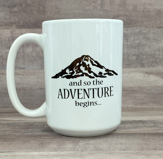 16oz ceramic mug, white base, with the phase and so the adventure begins with a artist image of Mount Rainier in black sublimated ink