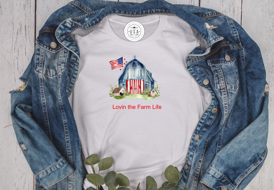 White unisex short sleeve TShirt with a red white and blue Americana barn and the saying Lovin the Farm Live in red