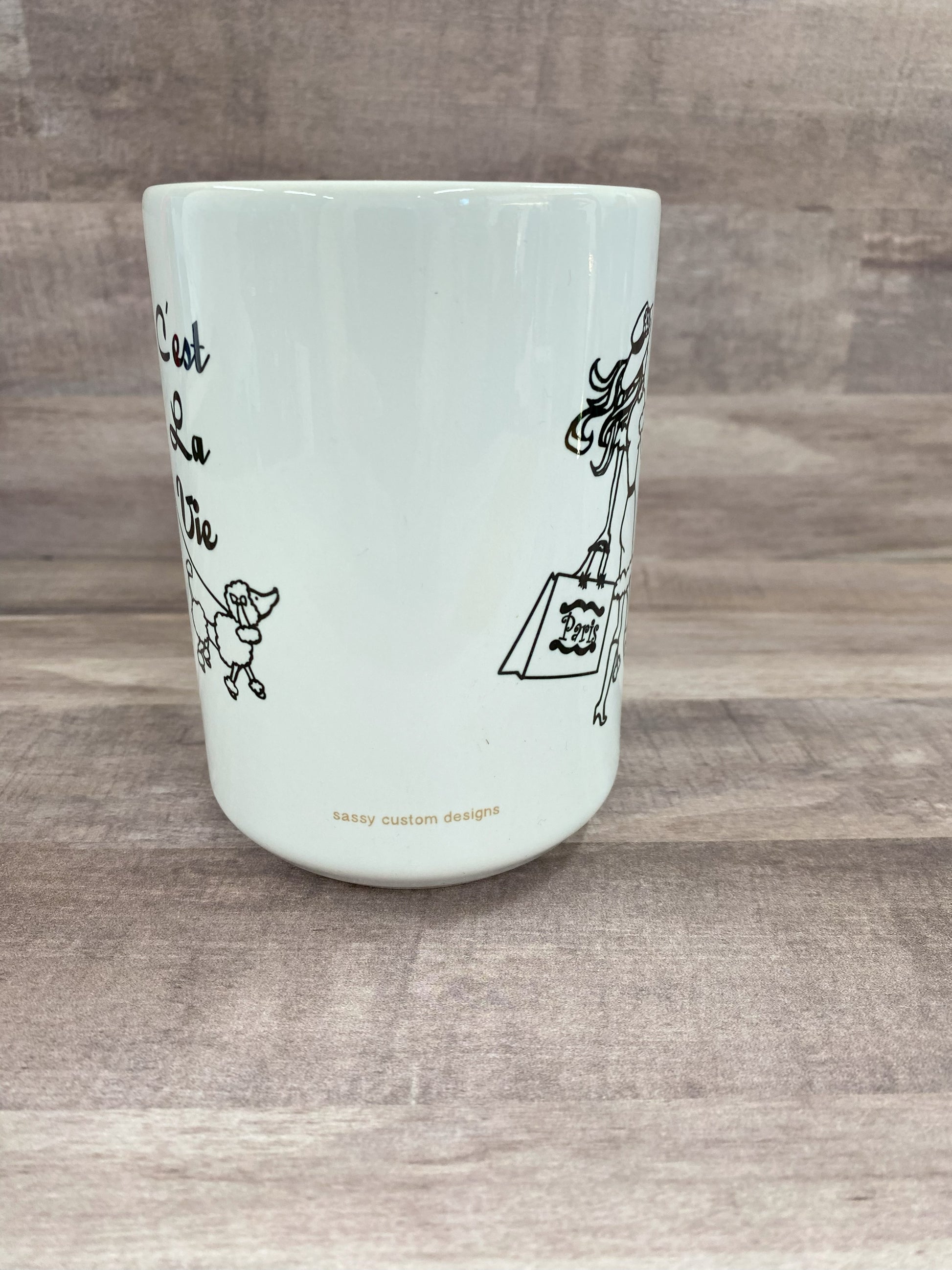 16oz cemaric white mug with the saying C'est la vie with an image of a woman carring shopping bags and walking a dog in blank sublimination ink.