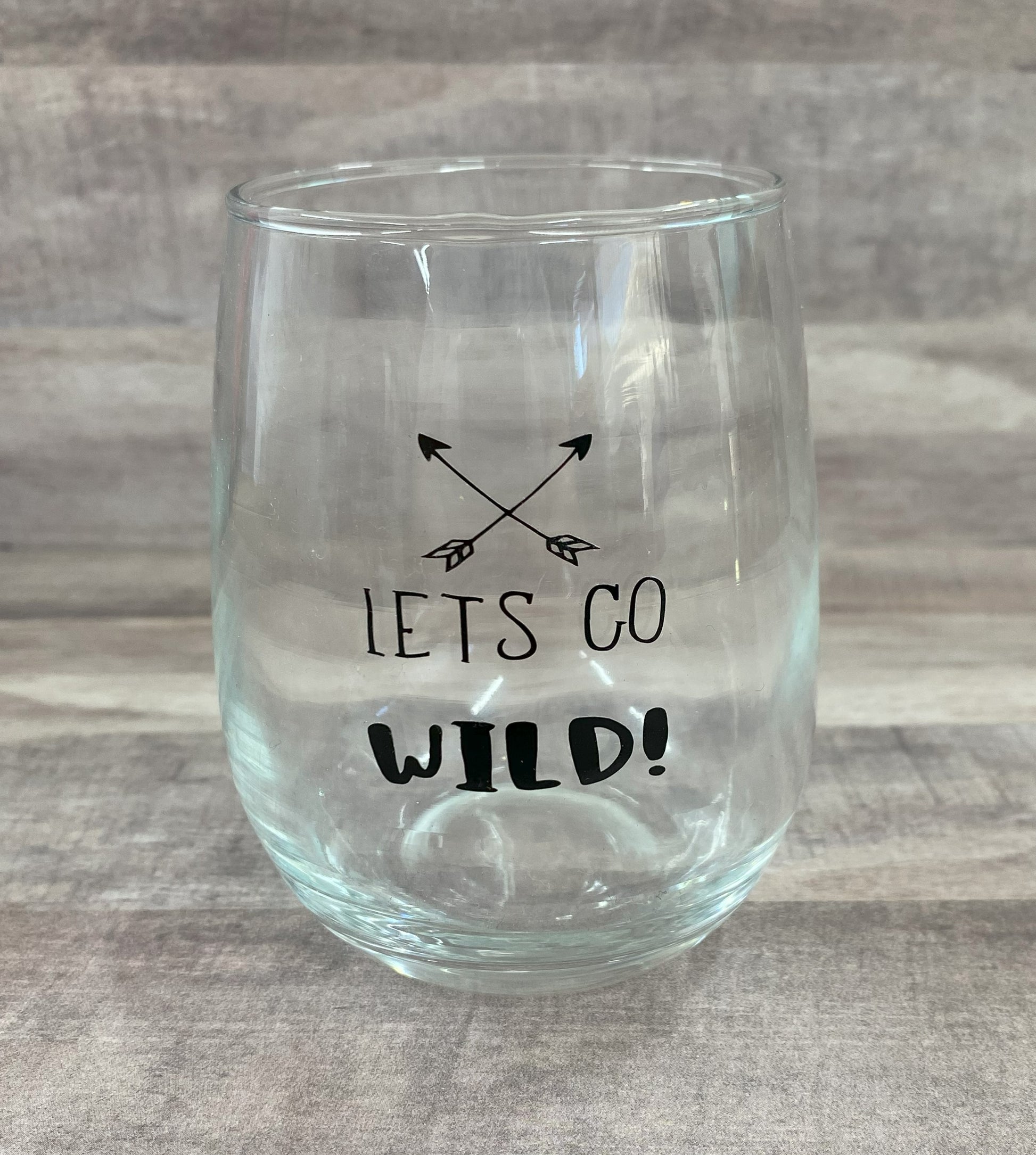 Stemless 15oz wine glass with the phrase lets go wild in black writing with crossed arrows Customizable. Designed by Grit City Rebel.