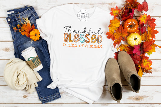 grit city rebel white unisex t-shirt with the phrase thankful blessed and kind of a mess.  Thankful is in black cursive, blessed is in fall colors with white dots, and kind of a mess is in orange. Available in sizes small to 3xl. 