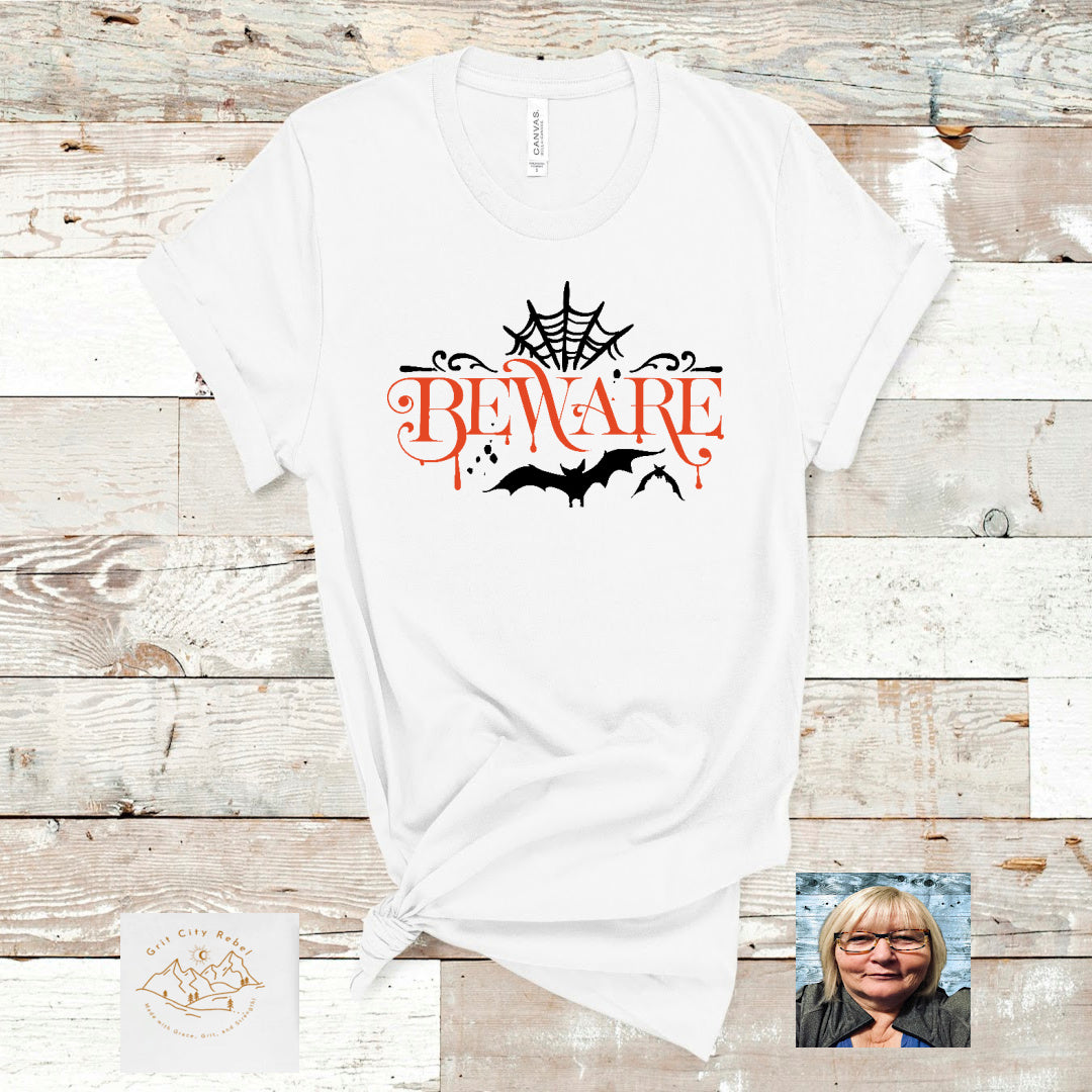 White unisex short sleeve T-Shirt with the word Beware and Halloween symbols around the word