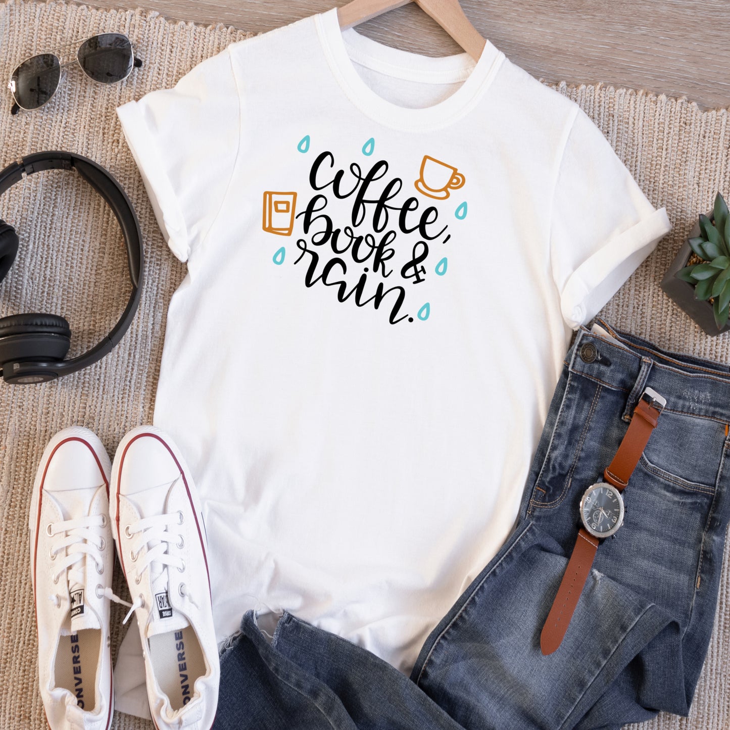White short sleeve Tshirt with the saying Coffe, Book & Rain in black with blue raindrops and a golden coffee mug