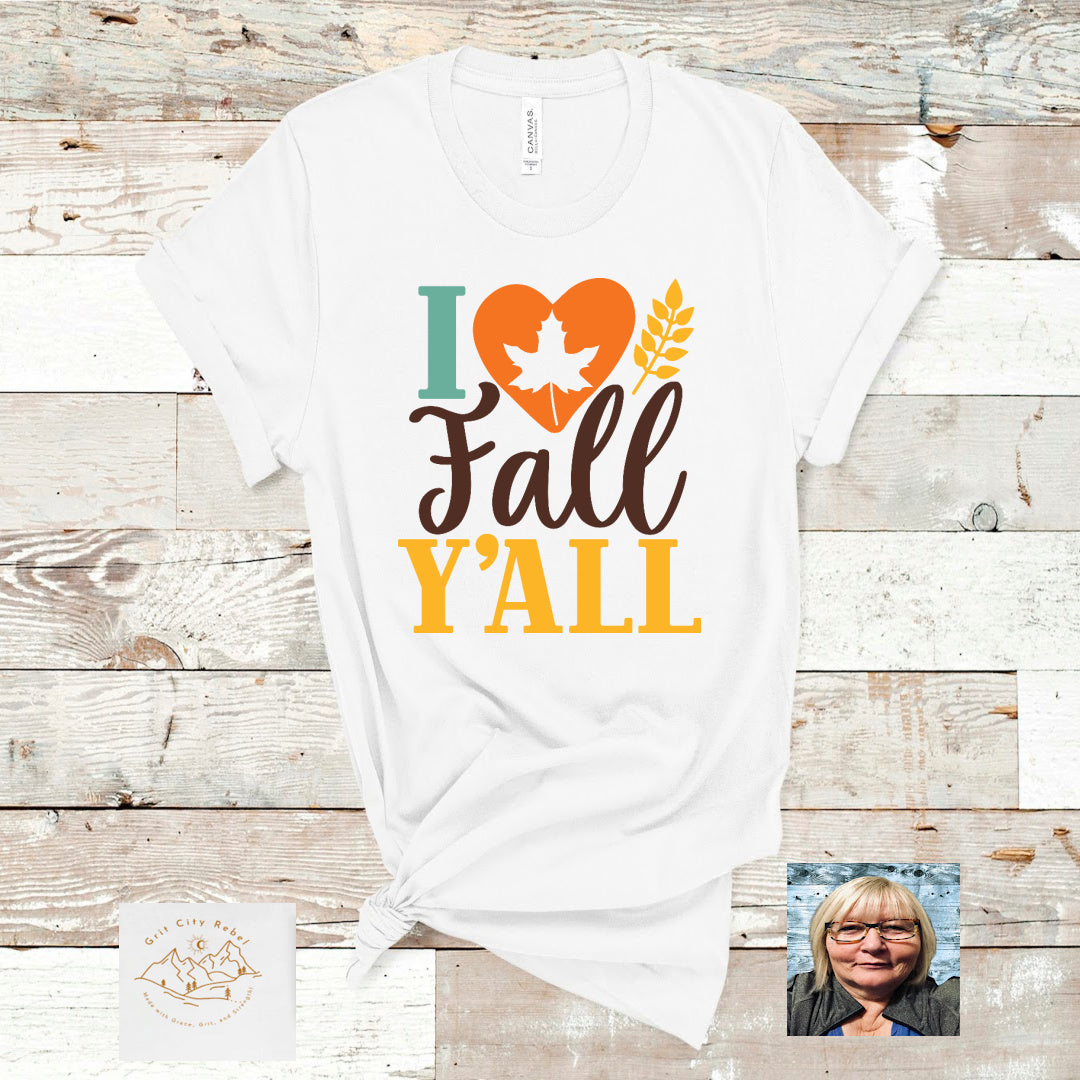 White unisex short sleeve Tshirt with a heart that has a leaf in it and the saying I love fall y'all in colors od teal orange yellow