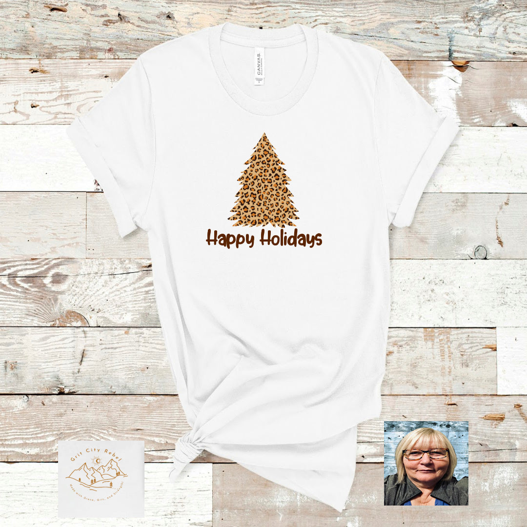 White T-Shirt with leopard print Trees and Happy Holidays in black writing.