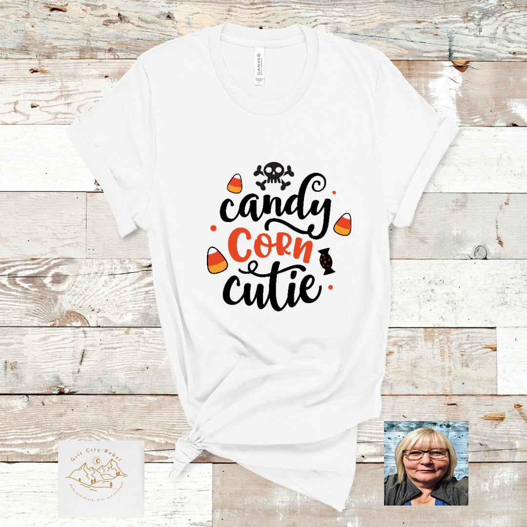 white unisex short sleeve TShirt with the saying Candy corn cutie in black and white has a skull and cross bones aboe the word candy